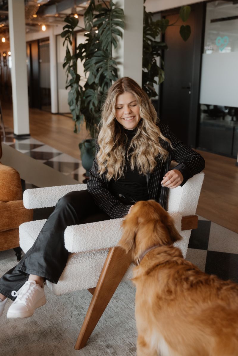 Eva sitting in an armchair, smiling at a golden retriever